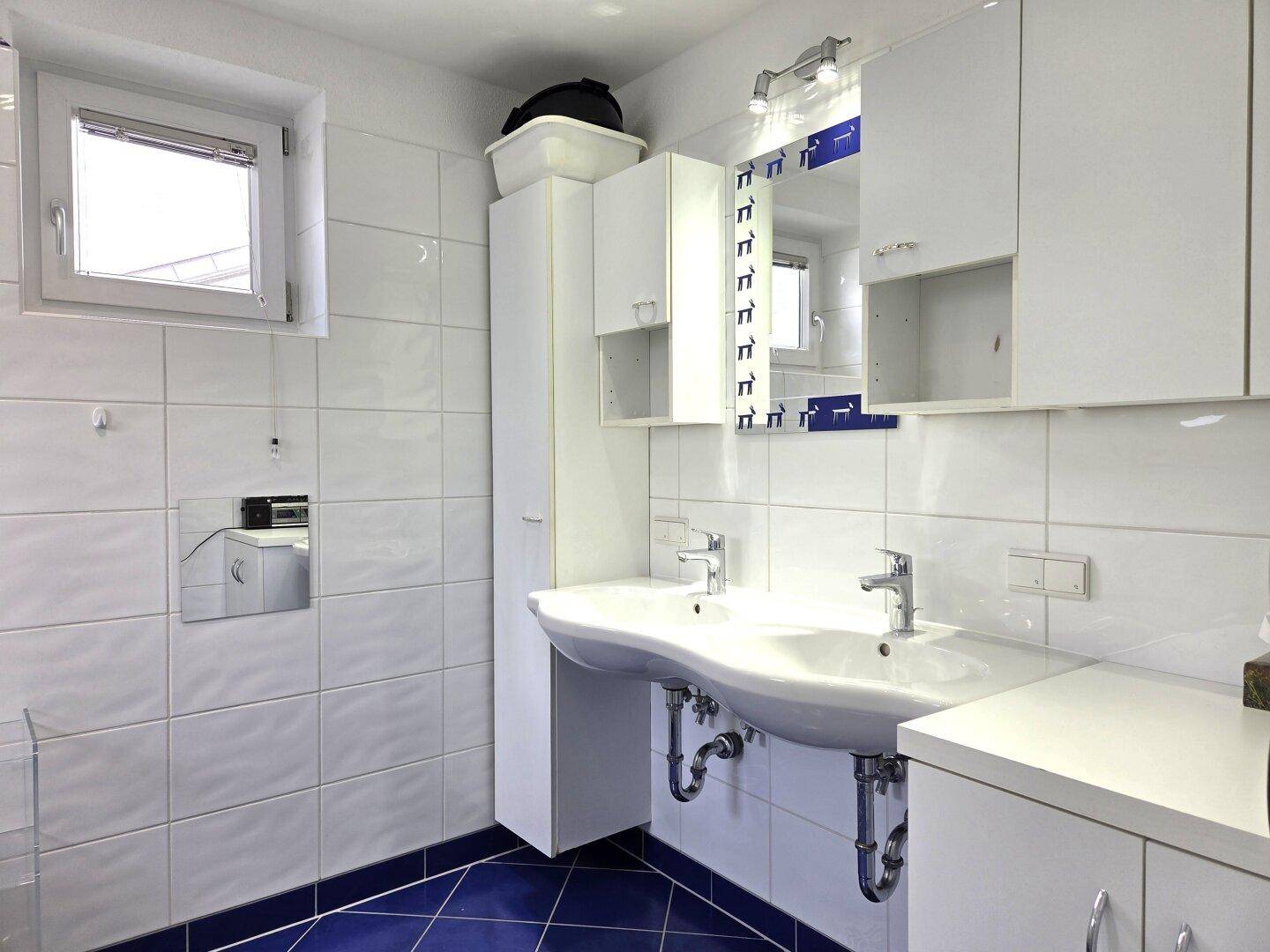 Modern gefliestes Badezimmer mit Doppelwaschbecken, Spiegelschrank und einem Fenster für Tageslicht.