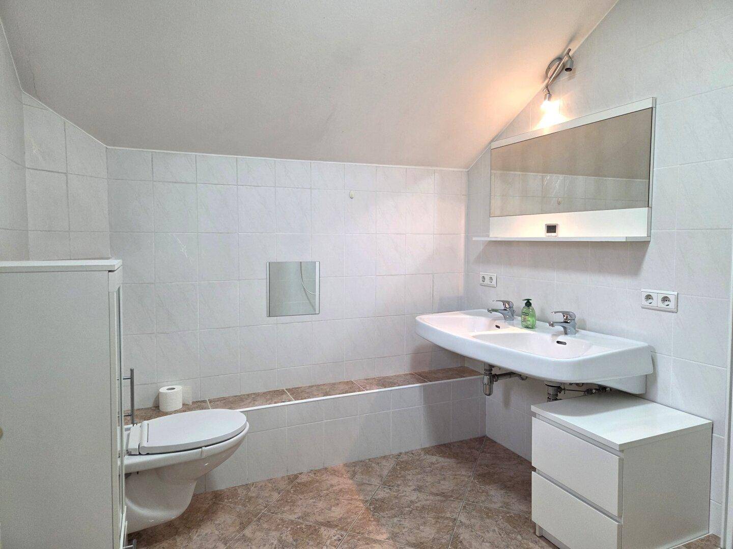 Geräumiges Badezimmer im Dachgeschoss mit Doppelwaschbecken, WC und hellen Fliesen.