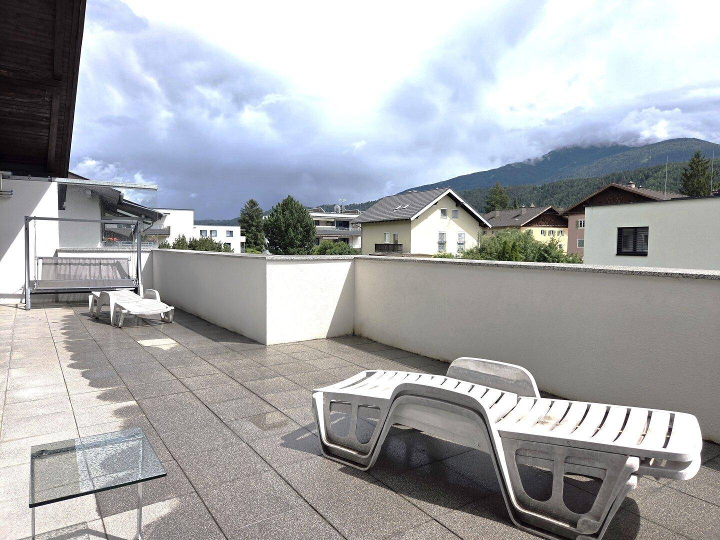Große Dachterrasse mit Liegestühlen und Blick auf die umliegenden Häuser und Berge.