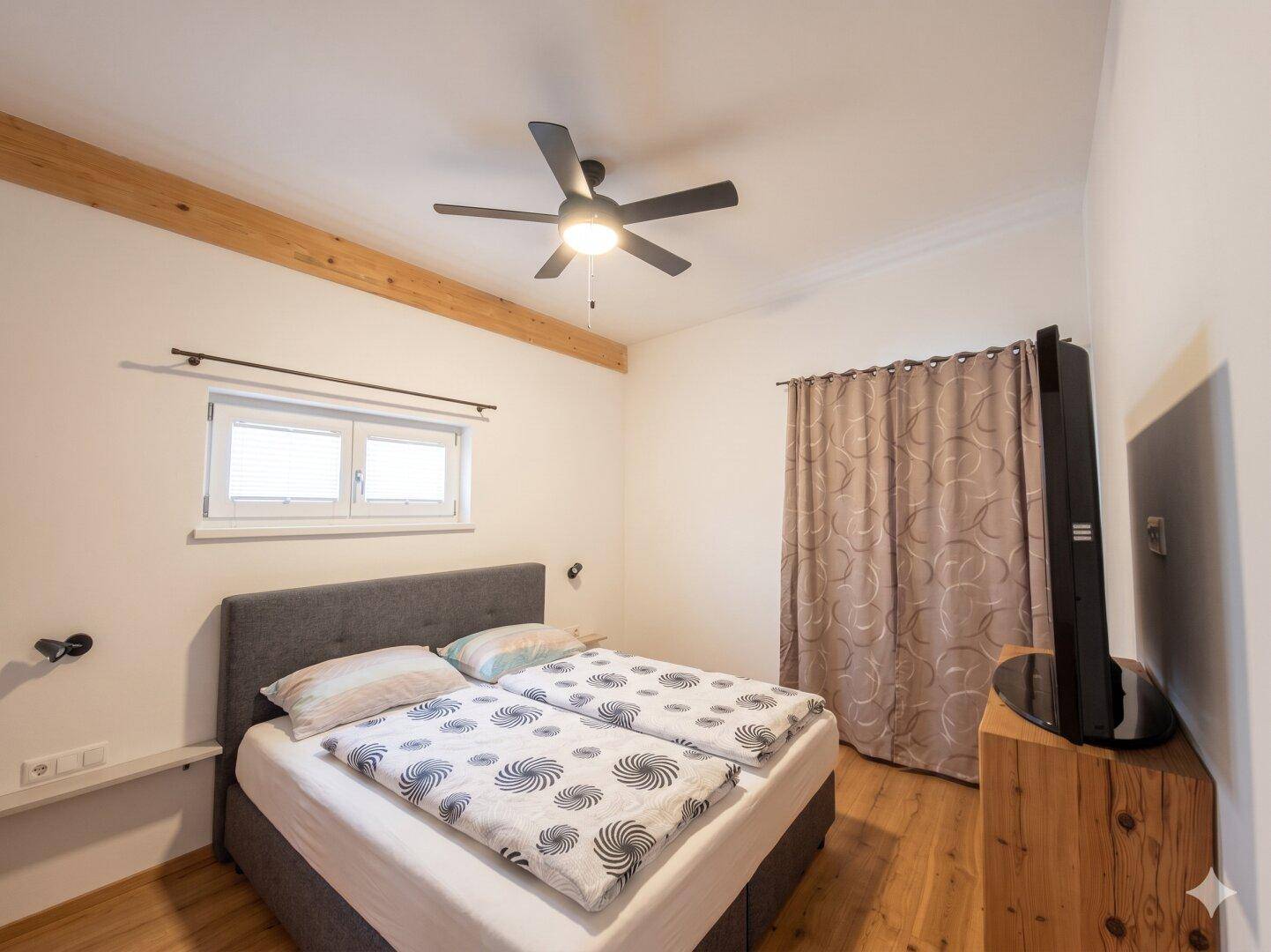Gemütliches Schlafzimmer mit Doppelbett, Holzbalken und Deckenventilator.