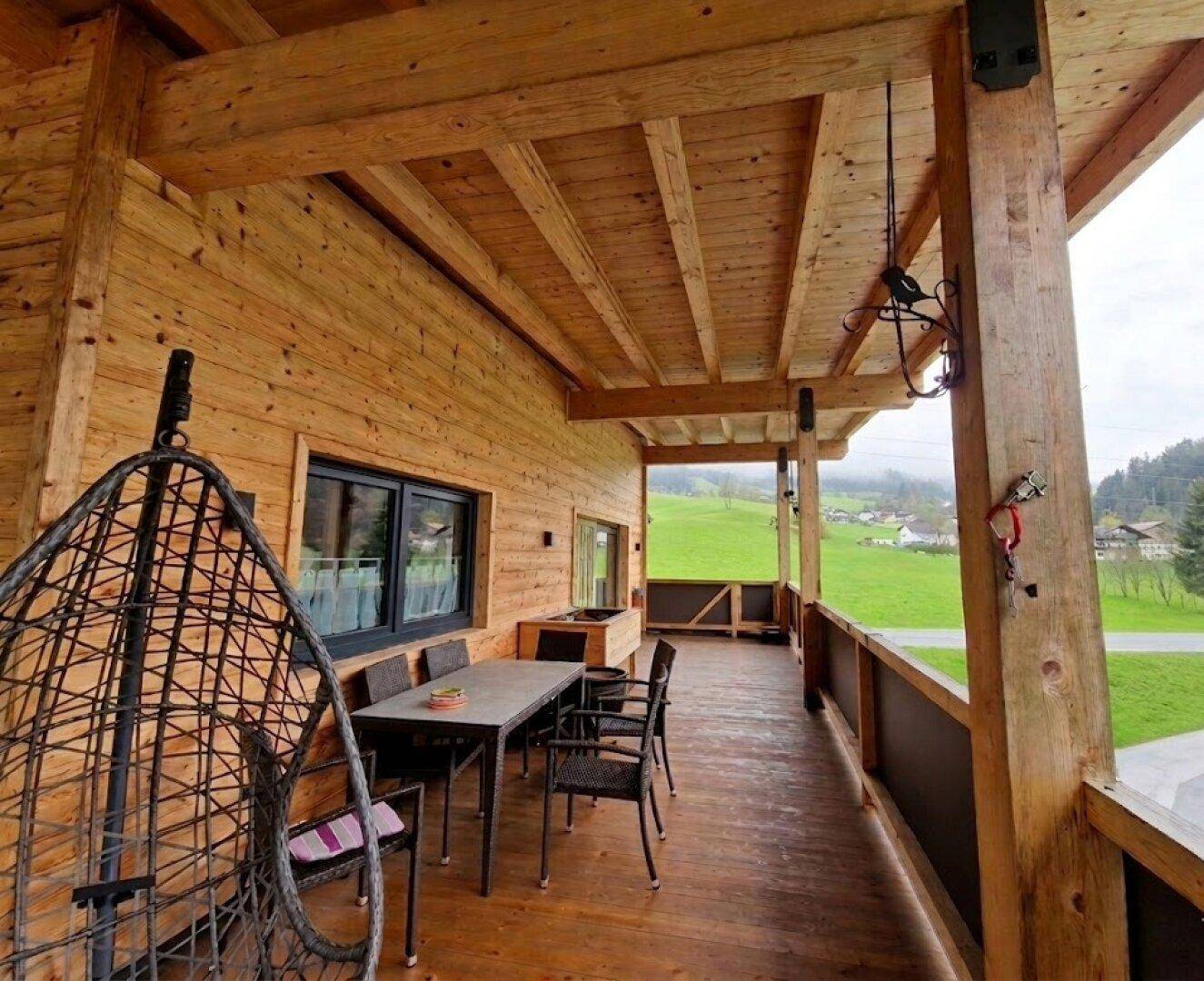 Großer überdachter Balkon mit Holzboden, Sitzbereich und weitem Blick ins Grüne.