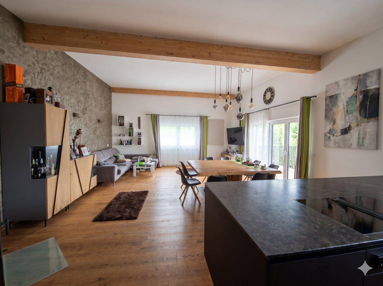 Geräumiger Wohn-Essbereich mit offener Küche, Holzbalken und Zugang zum Balkon.