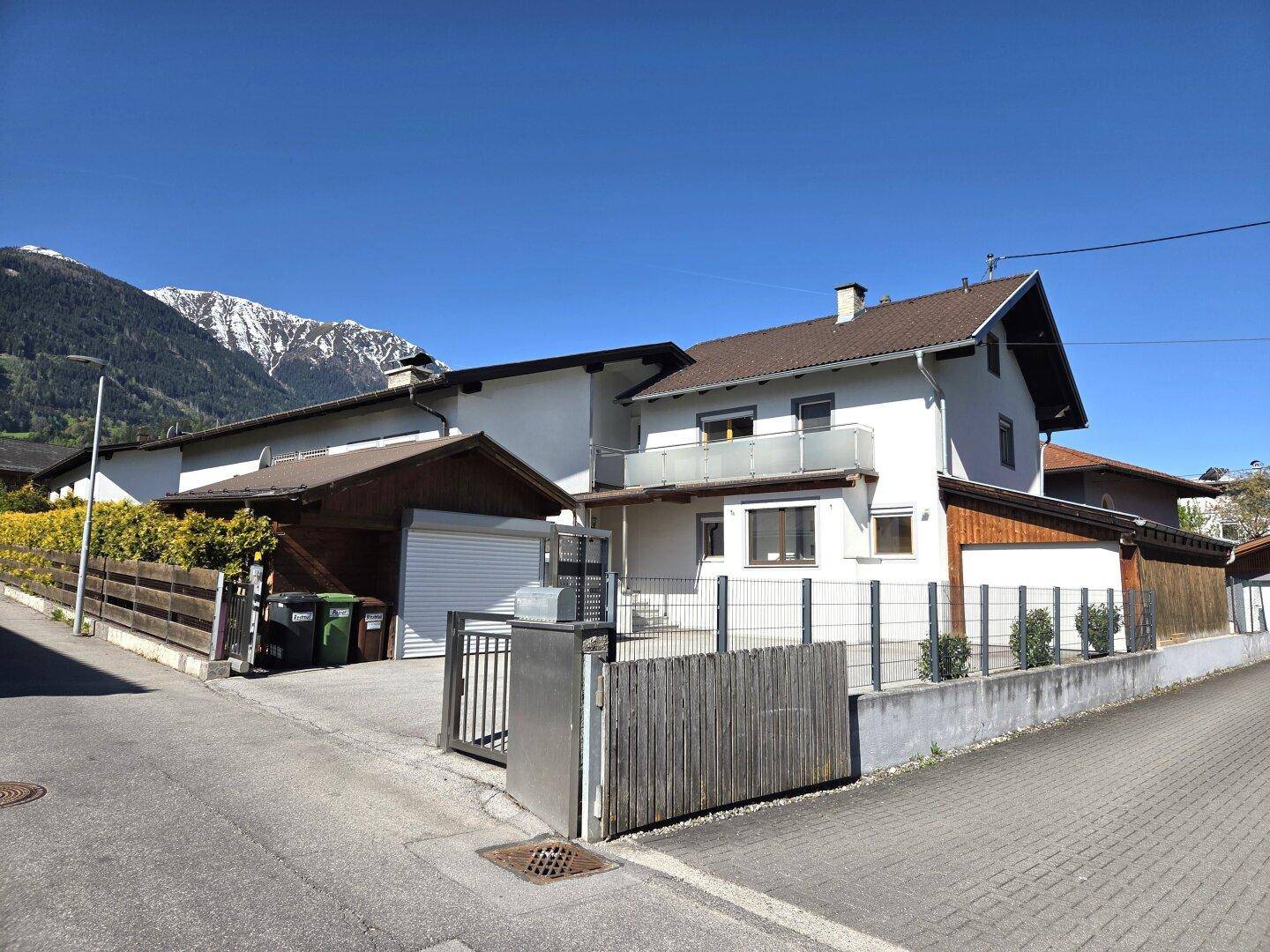 Wohnhaus mit weißer Fassade, braunem Dach und Balkon, umgeben von einer Berglandschaft.