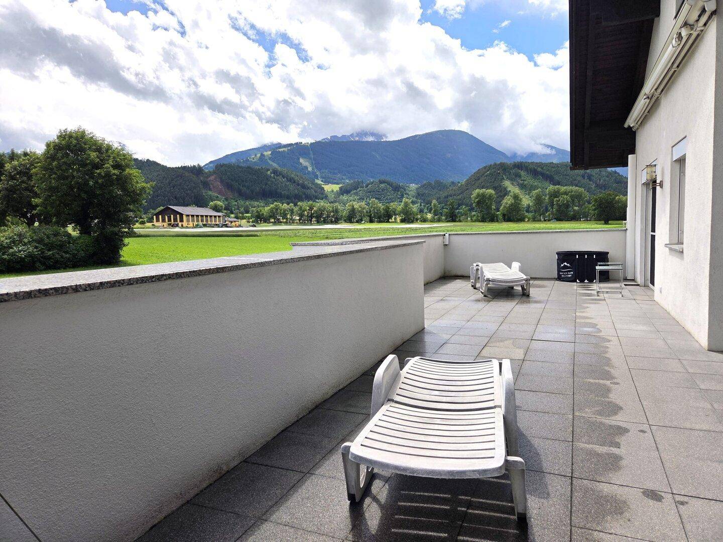 Weitläufige Terrasse mit Liegestühlen und Panoramablick auf die grüne Landschaft und die Berge.