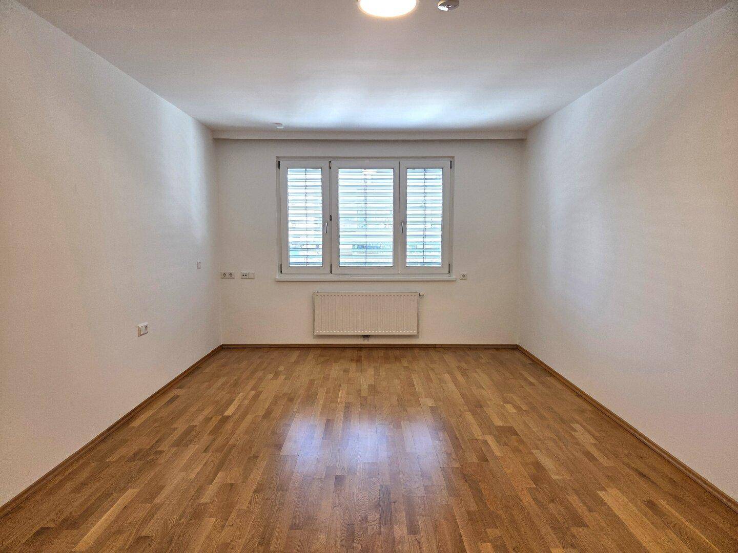 Geräumiger, heller Raum mit Parkettboden und großen Fenstern, ideal als Wohnzimmer nutzbar.