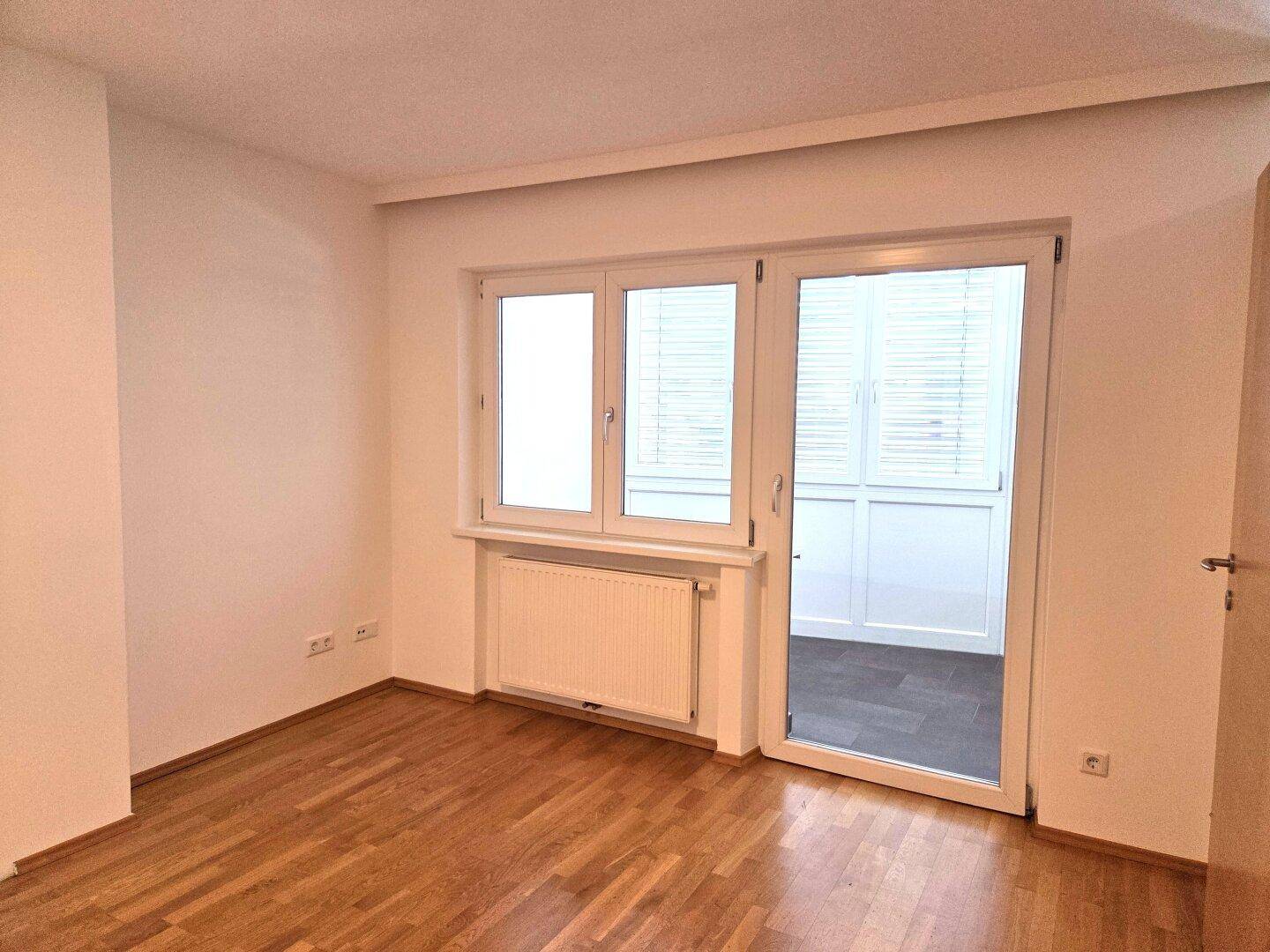 Helles Schlafzimmer mit Parkettboden und direktem Zugang zu einem überdachten Balkonbereich.