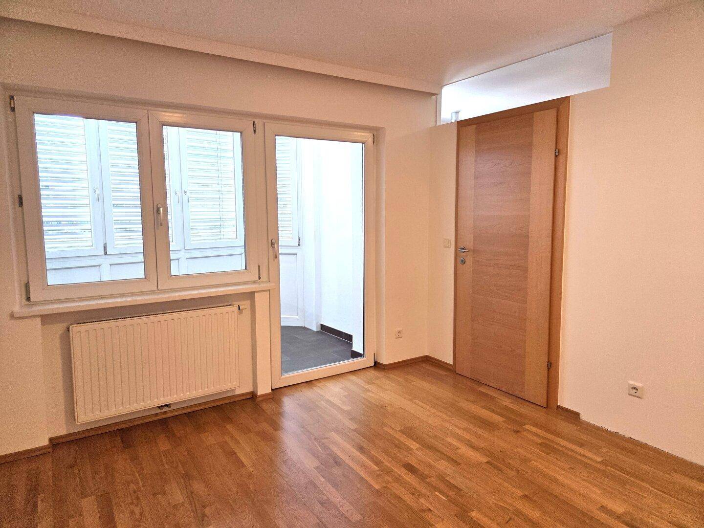 Lichtdurchflutetes Schlafzimmer mit Holzboden und Zugang zum Außenbereich, ausgestattet mit einer Holztür.