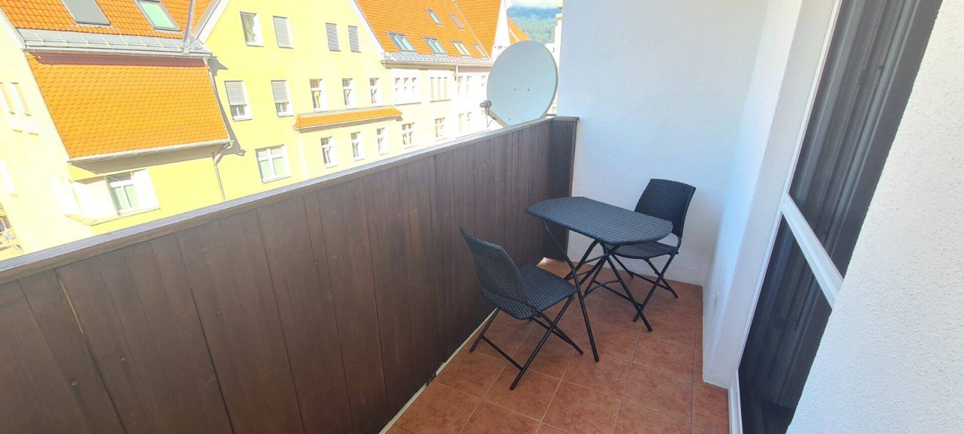 Gemütlicher Balkon mit kleinem Tisch und Stühlen, bietet einen Blick auf die umliegenden Gebäude.