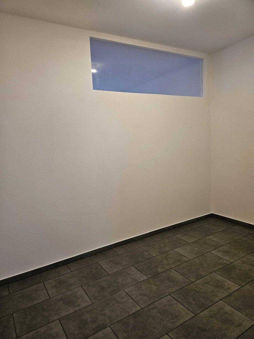 Kleiner Raum mit hoher Fensteröffnung und dunklen Fliesenboden, ideal als Abstellraum oder Hobbybereich.