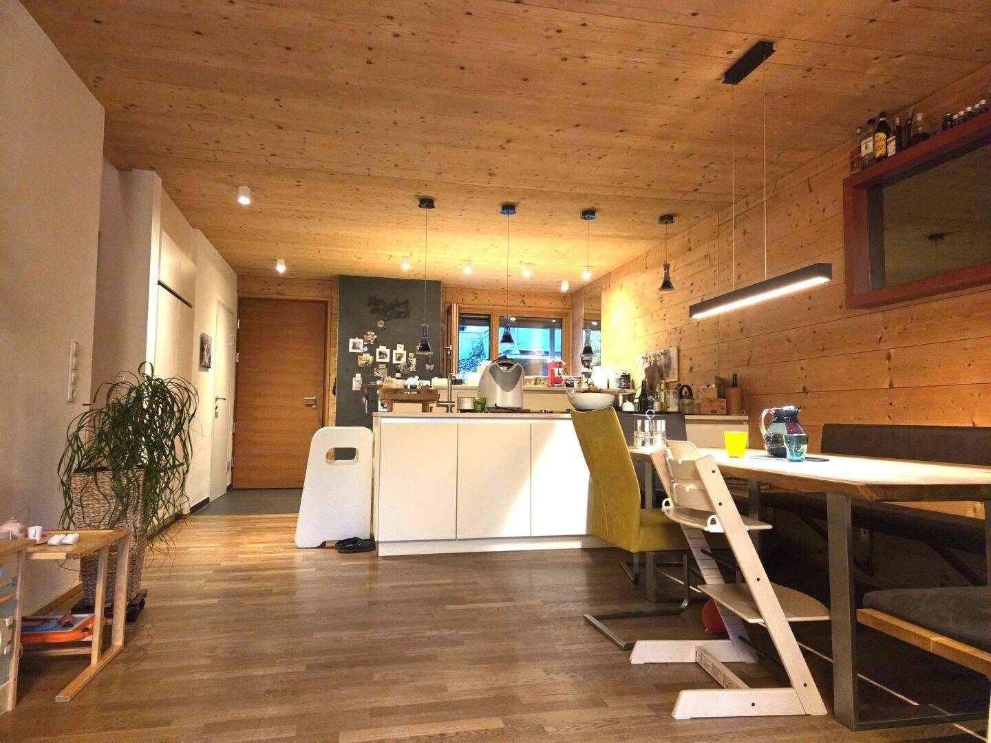 Moderne Küche mit Kochinsel und Essbereich, integriert in einen offenen Wohnraum mit Holzwänden.