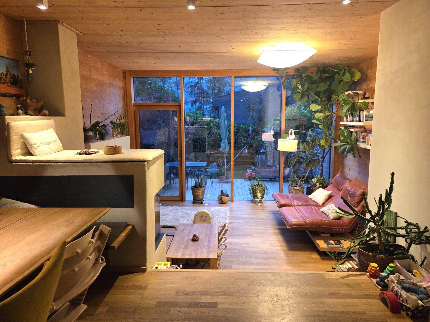 Heller Wohn- und Essbereich mit Holzböden, großen Glasfronten und Blick auf den grünen Garten.