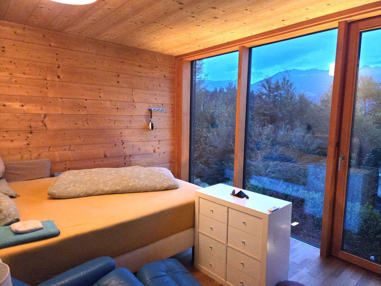 Schlafzimmer mit Holzwänden, großen Panoramafenstern und einem weiten Blick auf die Berge.