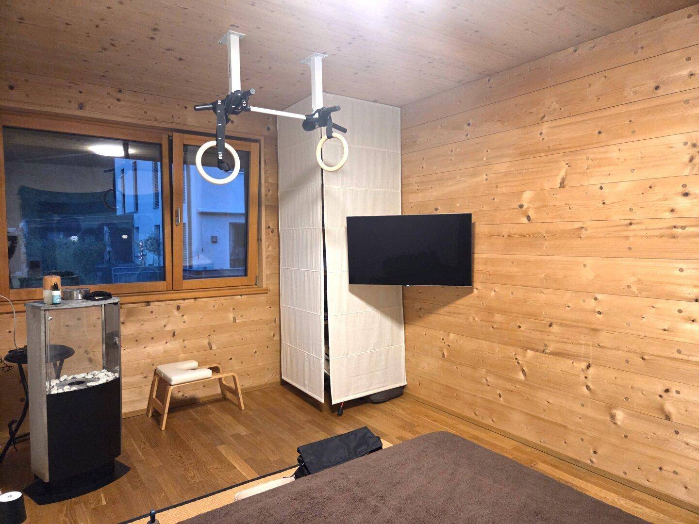 Schlafzimmer mit Holzwänden, einem Fernseher und integrierten Sportgeräten für aktive Bewohner.