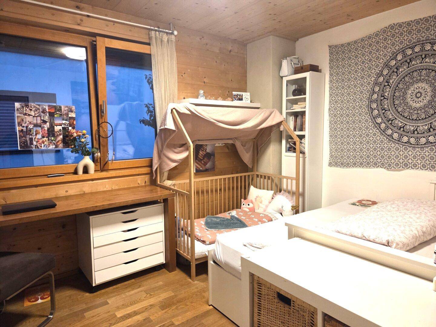 Kinderzimmer mit Holzwänden, Schreibtisch und einem gemütlichen Babybett, ideal für kleine Bewohner.