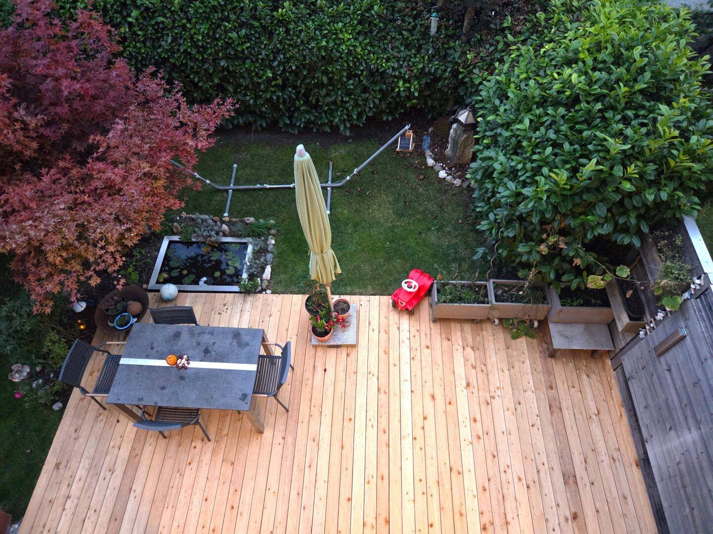 Vogelperspektive einer großen Holzterrasse mit Gartenmöbeln und angrenzendem grünen Garten.