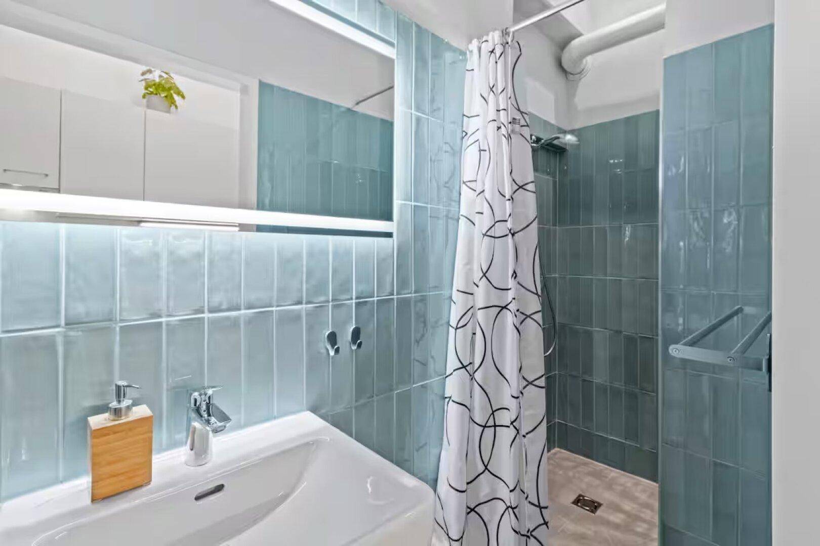 Modernes Badezimmer mit blauen Fliesen, begehbarer Dusche und minimalistischem Waschbecken.