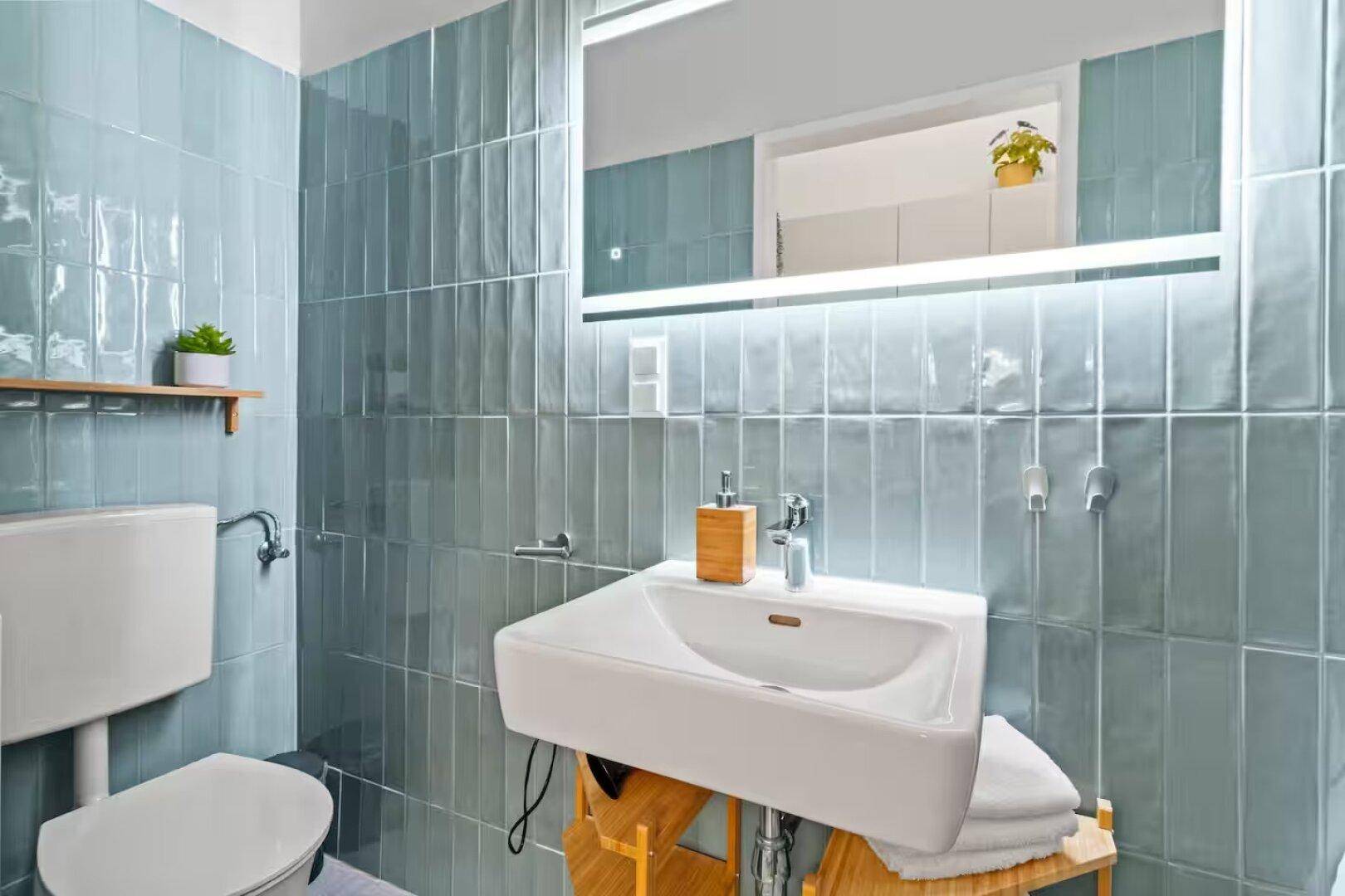 Helles Badezimmer mit blauen Wandfliesen, modernem Waschbecken und Toilette.