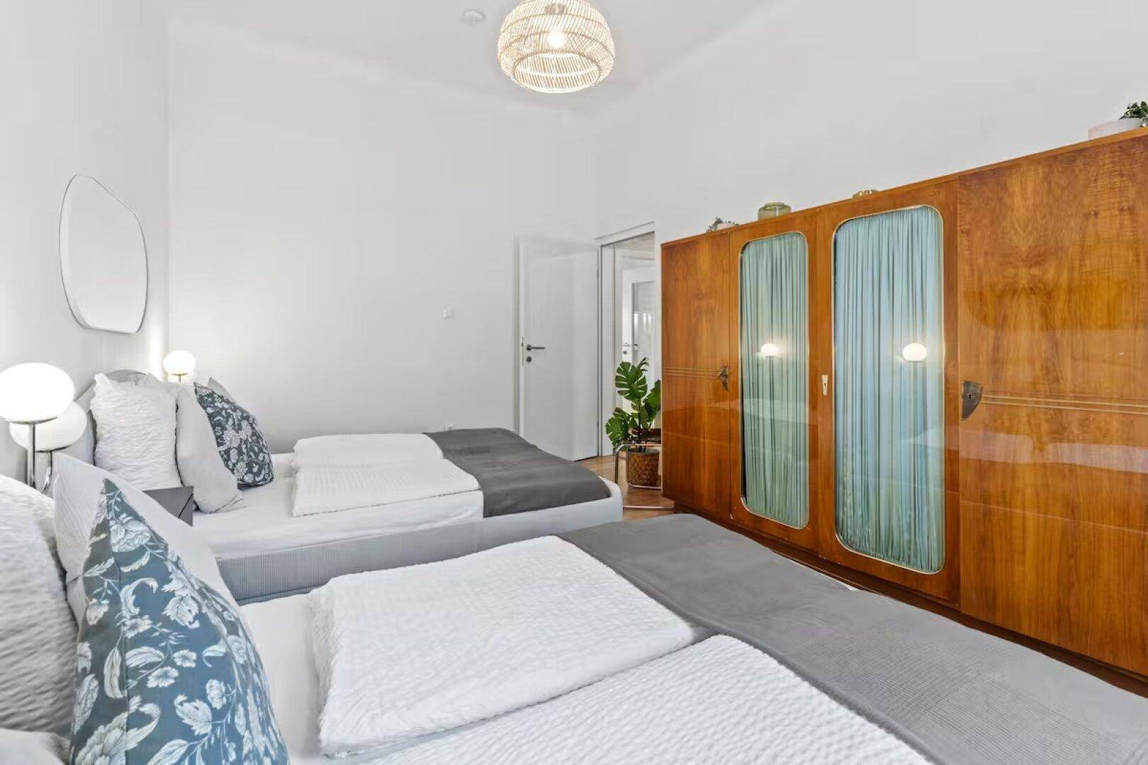 Helles Schlafzimmer mit zwei Betten und einem großen, antiken Holzschrank.
