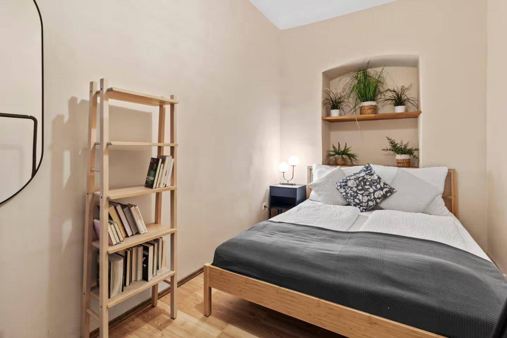 Gemütliches Schlafzimmer mit Holzbett, Bücherregal und dekorativen Pflanzen in einer Nische.
