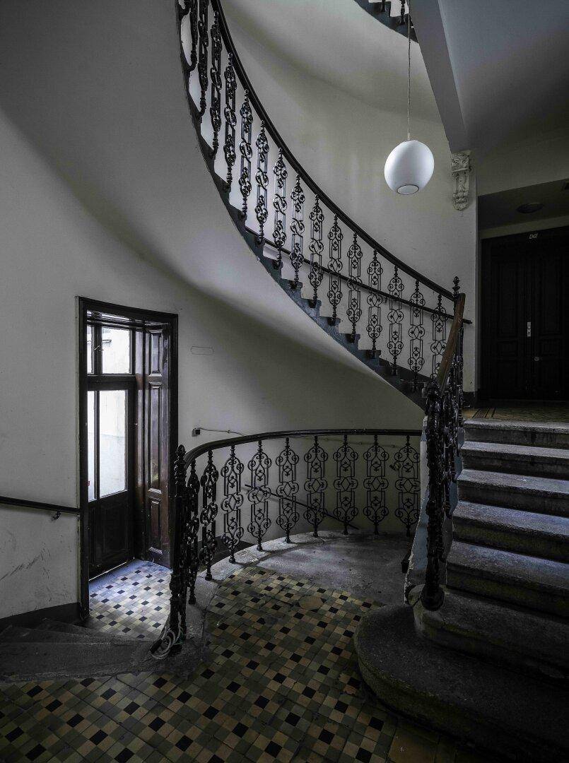 Elegantes Treppenhaus mit geschwungener schmiedeeiserner Balustrade und gemusterten Fliesen.