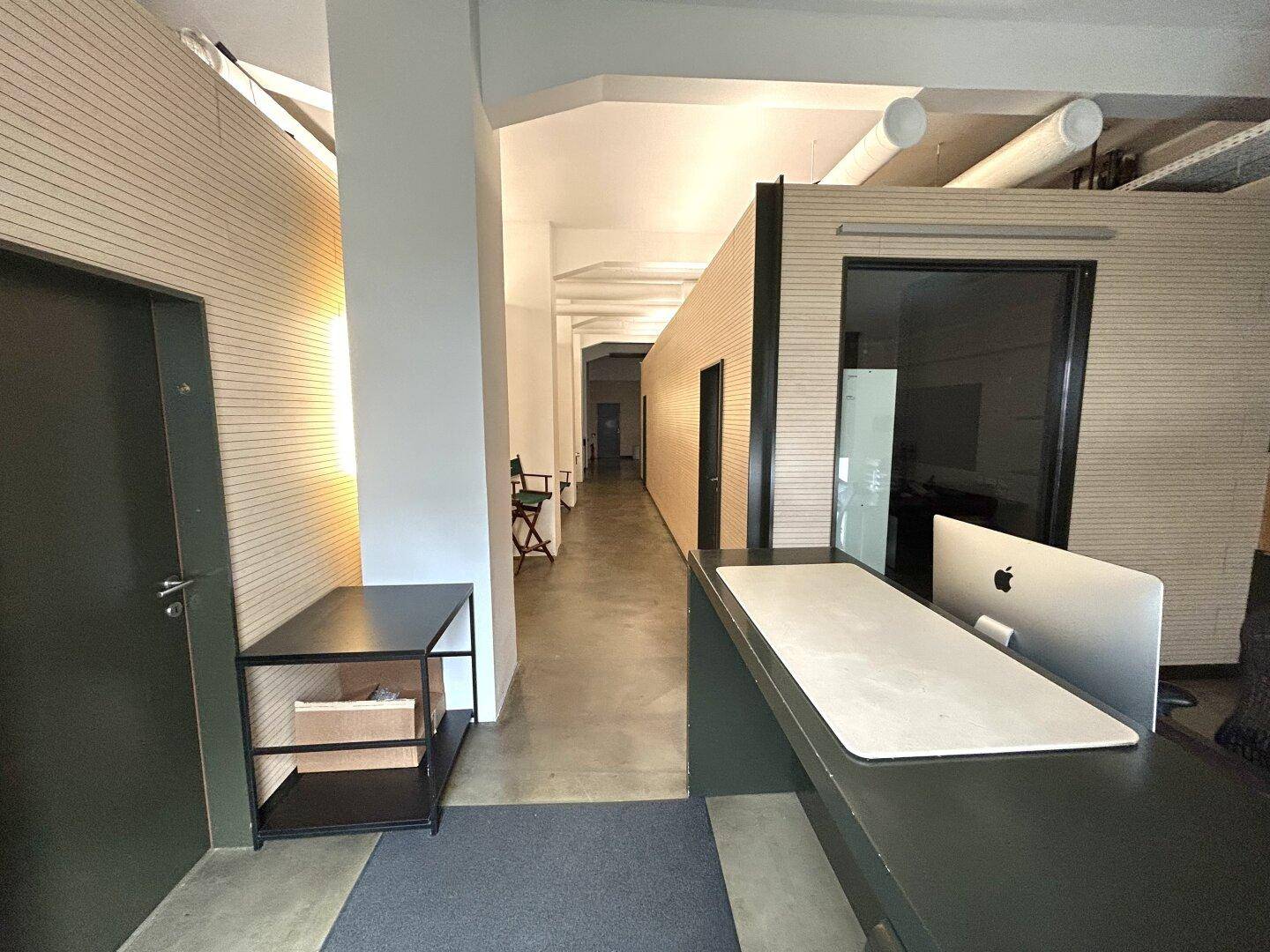Langer Flur mit Empfangsbereich, Holzvertäfelung und industriellem Design mit sichtbaren Deckenleitungen.