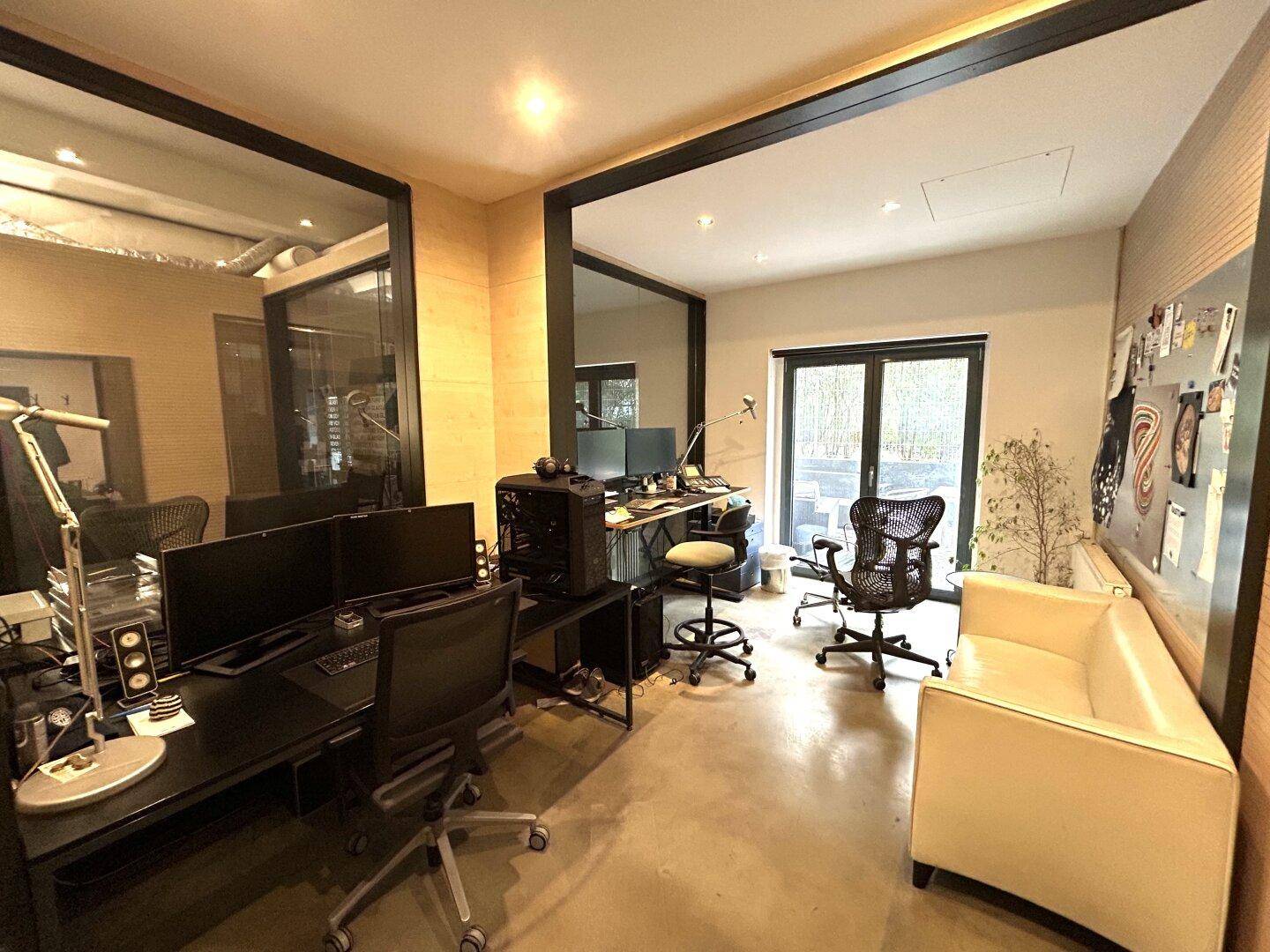Modernes Büro mit mehreren Arbeitsplätzen, großen Fenstern und stilvoller Holzvertäfelung an den Wänden.