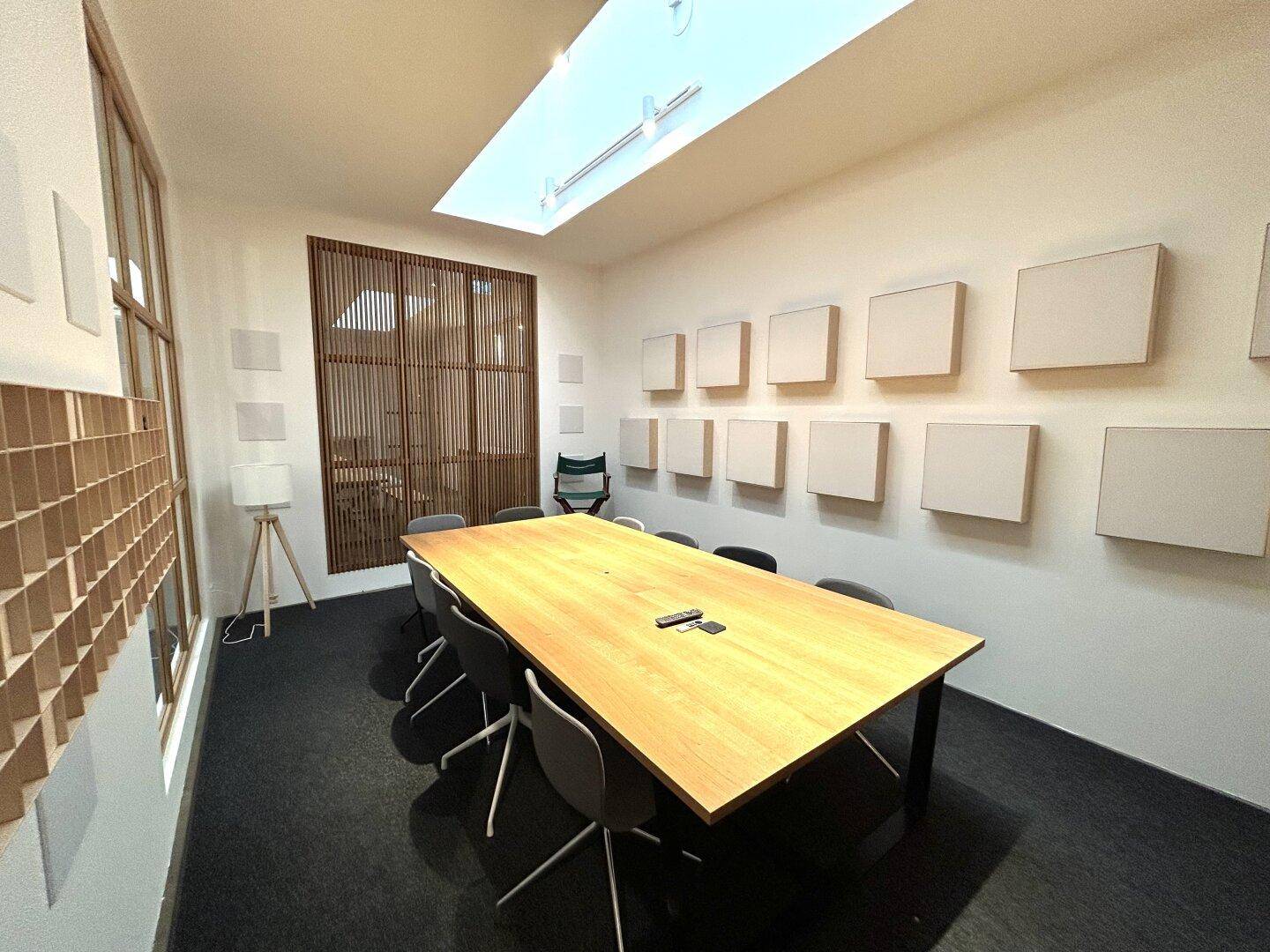 Konferenzraum mit großem Holztisch, Deckenfenster und dekorativen Holzlamellen an der Wand.