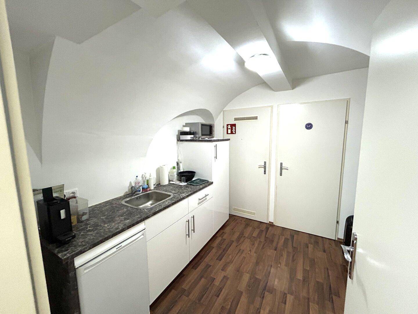 Kleine Küchenzeile mit Spüle, Mikrowelle und Kühlschrank unter einer markanten gewölbten Decke.