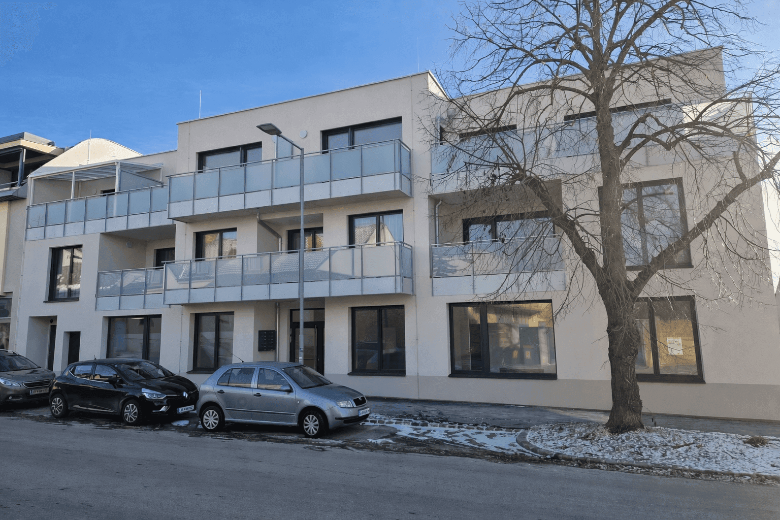 Moderne Wohnanlage mit mehreren Balkonen und großen Fenstern an einem sonnigen Wintertag.