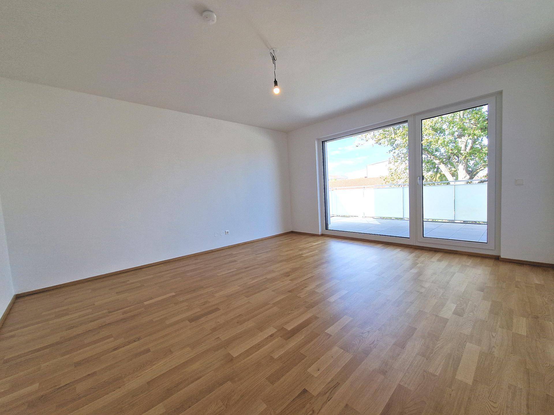 Helles Zimmer mit Parkettboden und großer Fensterfront, die viel Tageslicht hereinlässt.