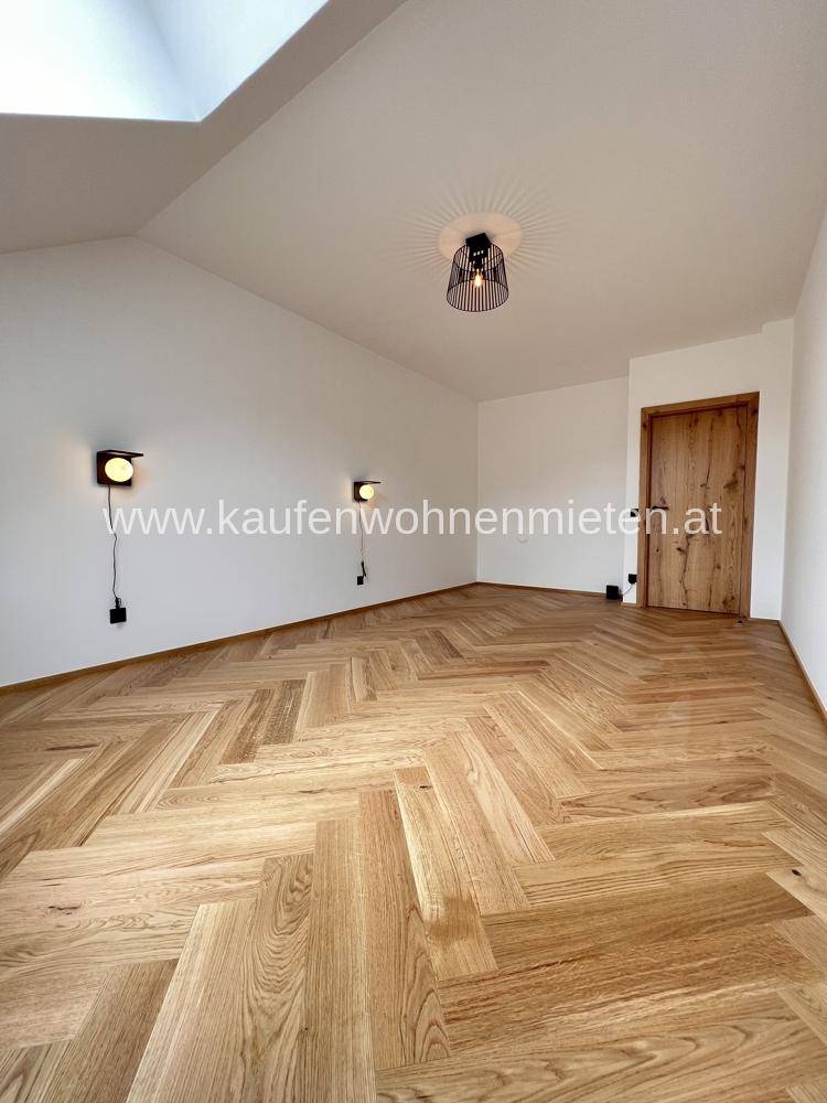 Geräumiges Schlafzimmer mit Dachschräge, Fischgrätparkettboden und modernen Wandleuchten.