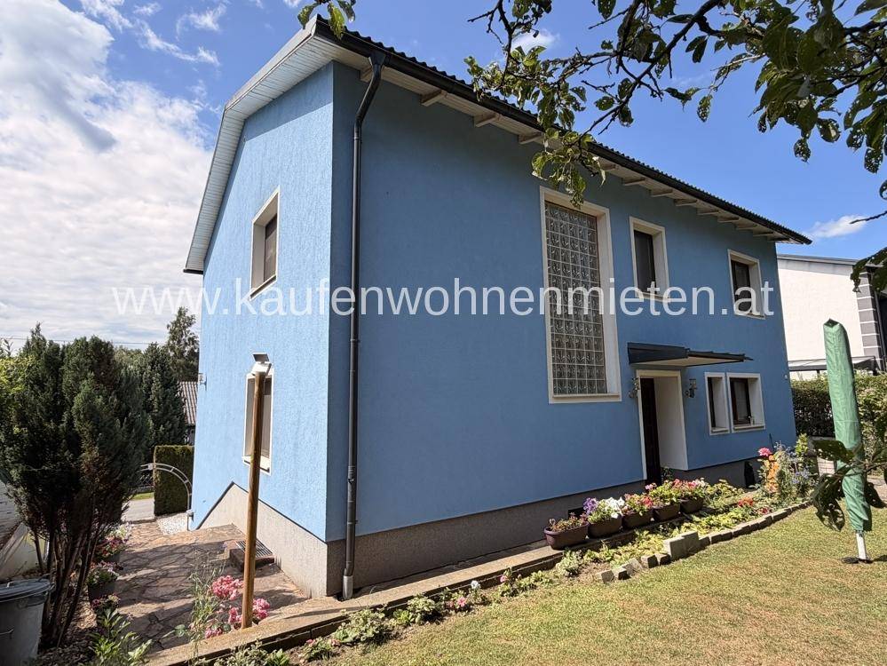 Seitenansicht des blauen Hauses mit großen Fenstern und Zugang zum Gartenbereich.
