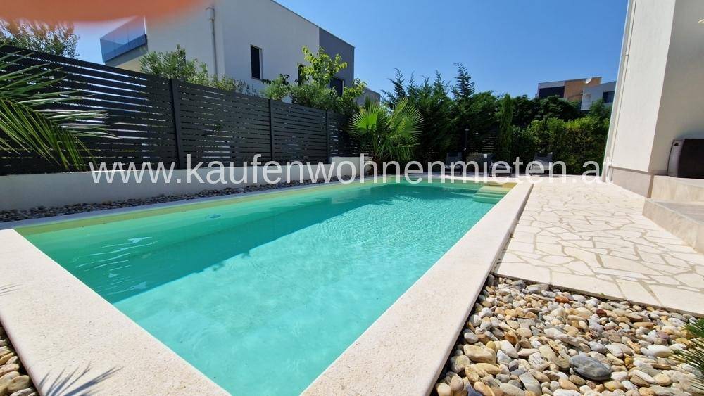 Langer Swimmingpool mit Kiesumrandung und moderner Zaunanlage im Außenbereich der Villa.