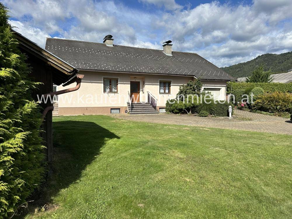 Einfamilienhaus mit gepflegtem Vorgarten und Zufahrt, umgeben von grüner Landschaft.