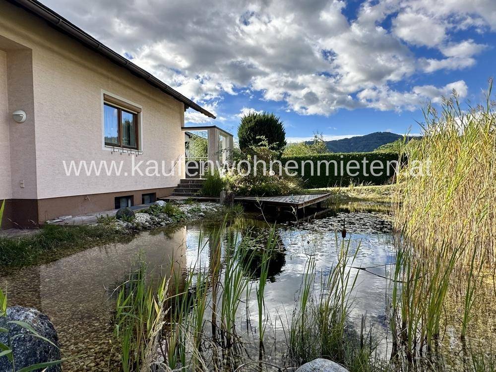 Natürlicher Gartenteich mit Holzsteg und üppiger Bepflanzung neben dem Haus.