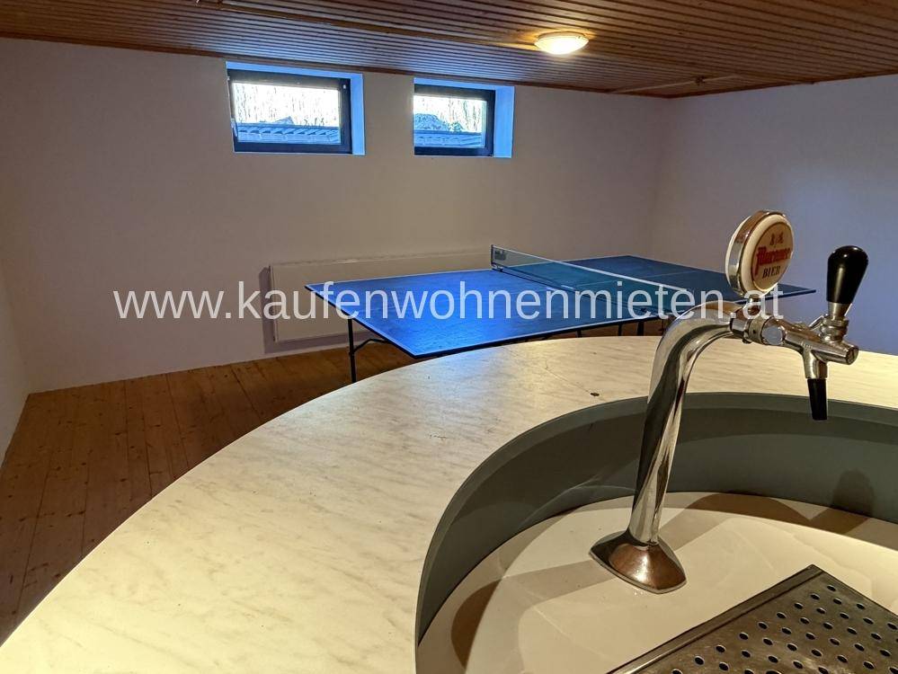 Freizeitraum mit Tischtennisplatte und Barbereich, ausgestattet mit Holzboden und kleinen Fenstern.