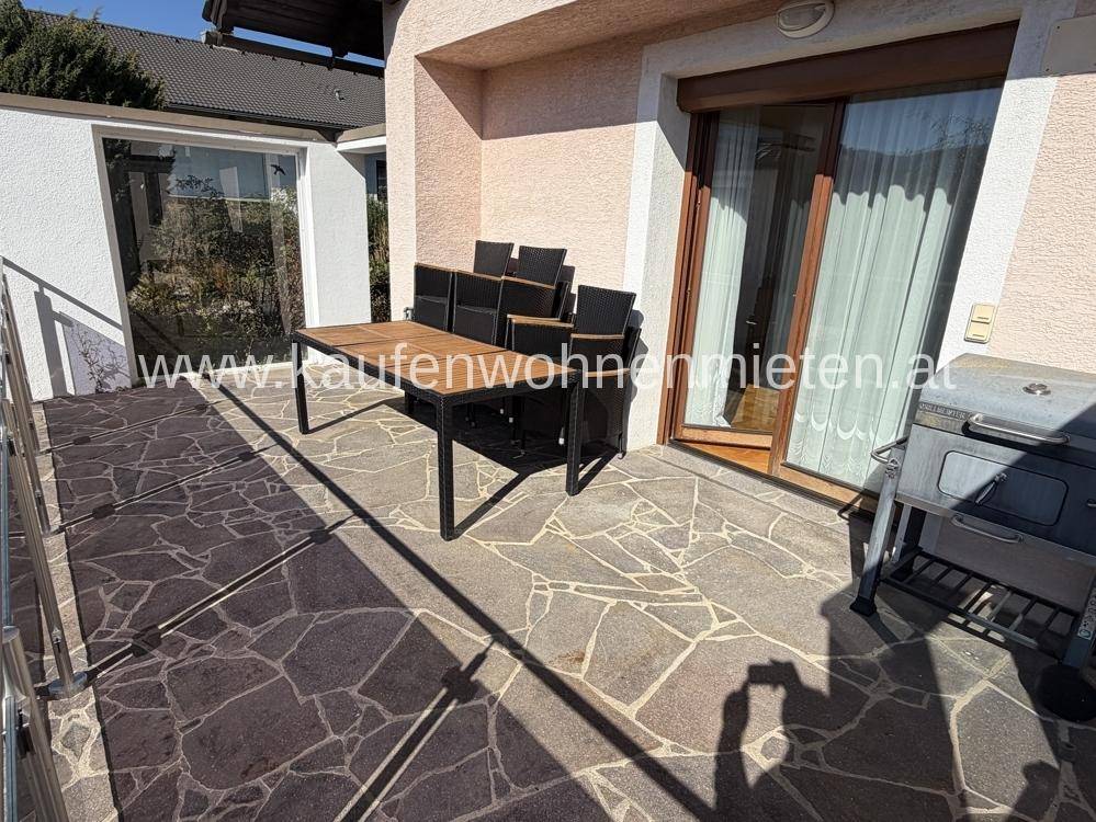 Geräumige Terrasse mit Steinplattenboden, Esstisch und Grill, ideal für Mahlzeiten im Freien.