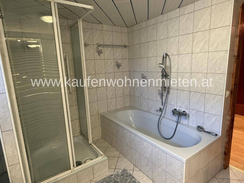 Badezimmer mit Badewanne, Duschkabine und hellen Fliesen, funktional eingerichtet.