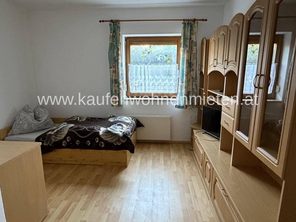 Schlafzimmer mit Holzboden, Einzelbett und traditionellen Holzmöbeln, hell durch Fenster.