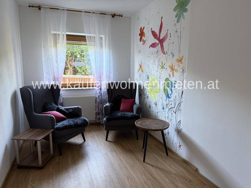 Helles Zimmer mit Laminatboden, farbenfroher Wanddekoration und zwei bequemen Sesseln.