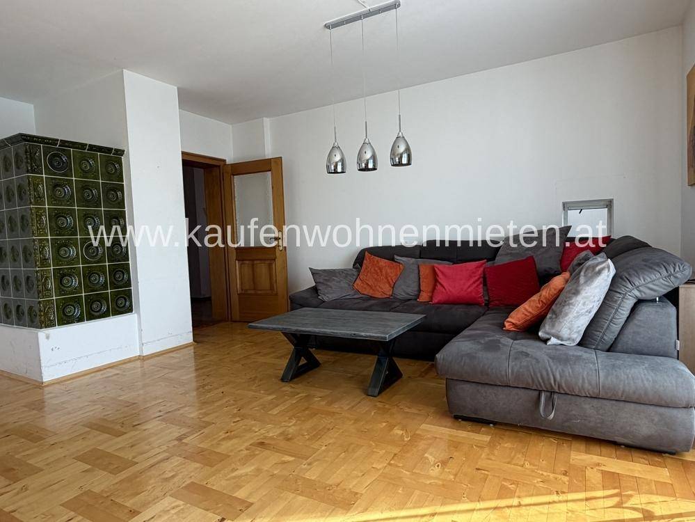 Gemütliches Wohnzimmer mit Kachelofen, Parkettboden und großem Ecksofa.