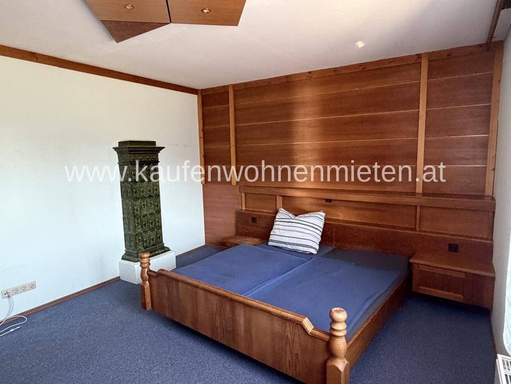 Schlafzimmer mit traditionellem Kachelofen, Holzbett und Holzvertäfelung an der Wand.