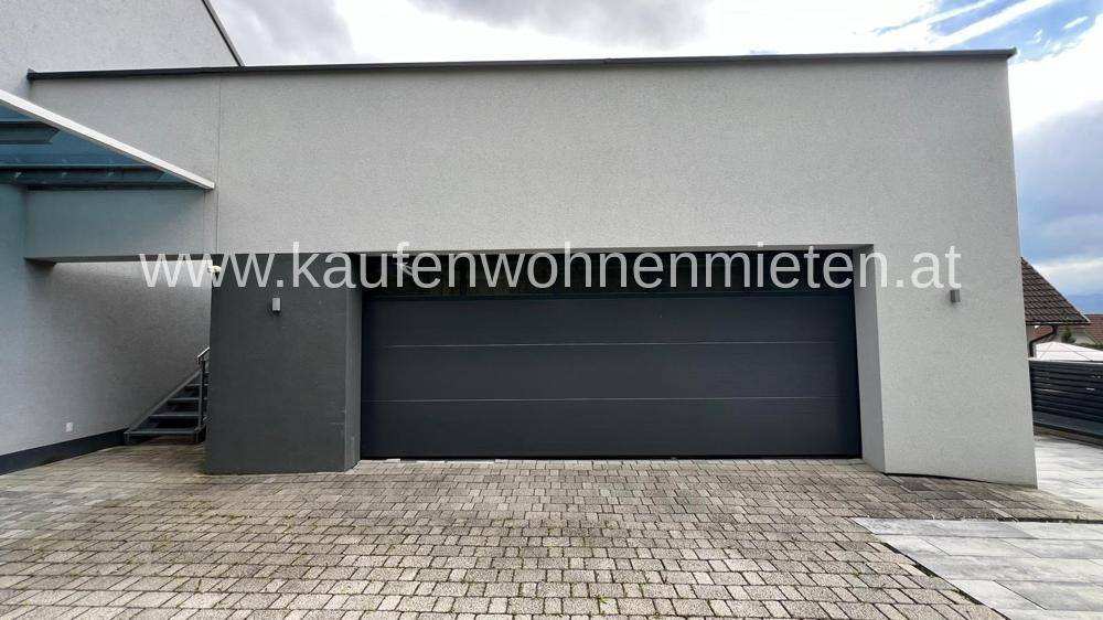 Moderne Doppelgarage mit dunklem Tor und gepflasterter Zufahrt an einem Neubau.
