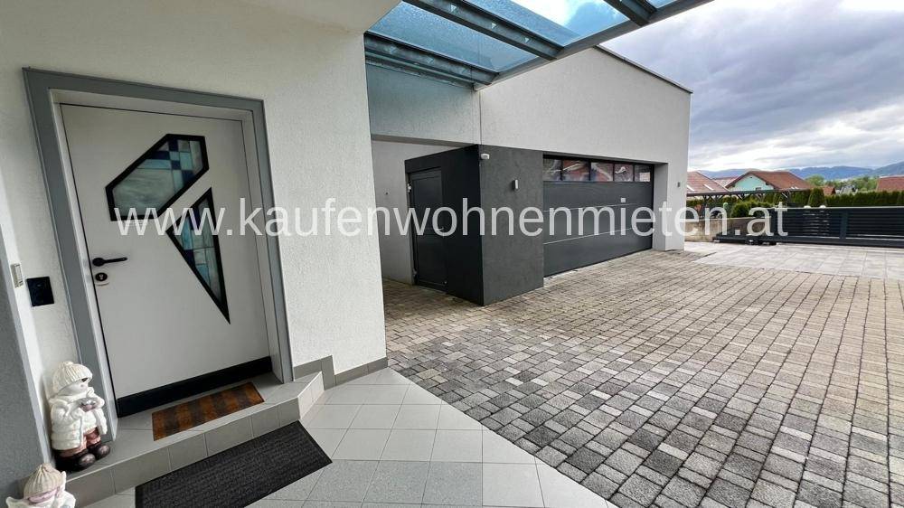 Moderner Eingangsbereich mit gepflasterter Auffahrt und integrierter Garage unter einem Glasvordach.