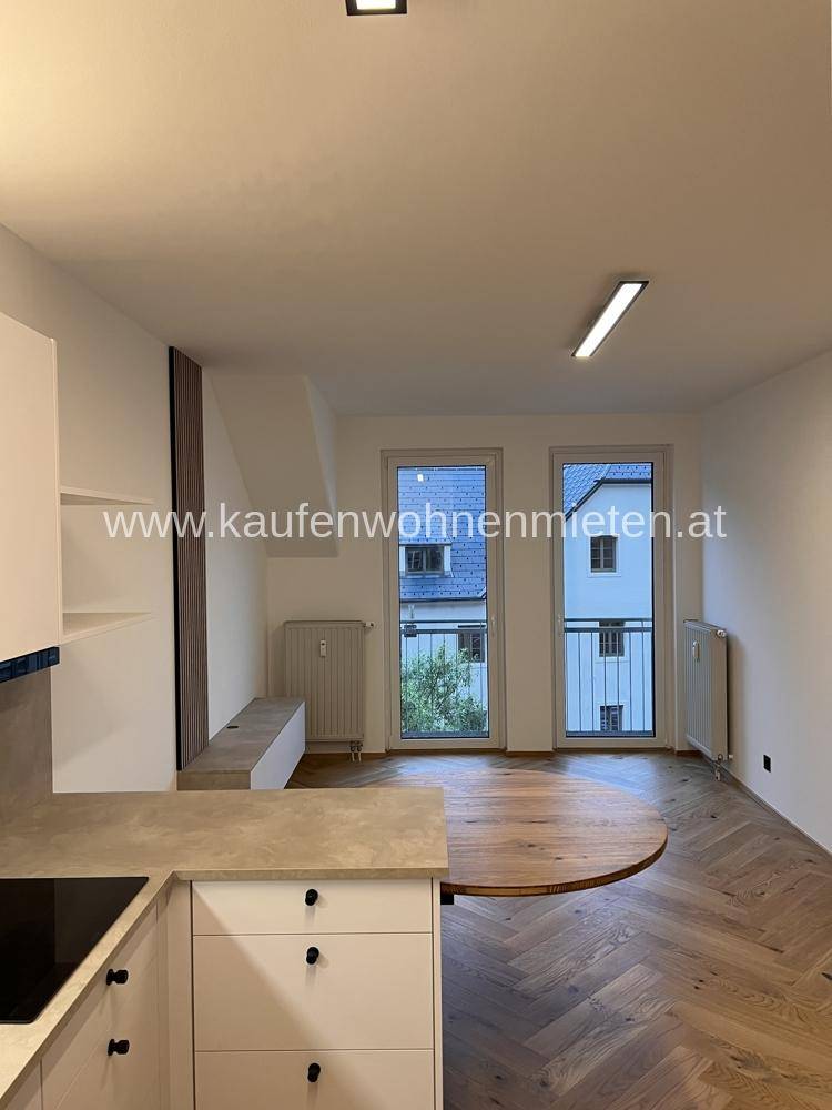 Wohnbereich mit Fischgrätparkett und Zugang zu einem französischen Balkon mit Blick ins Grüne.