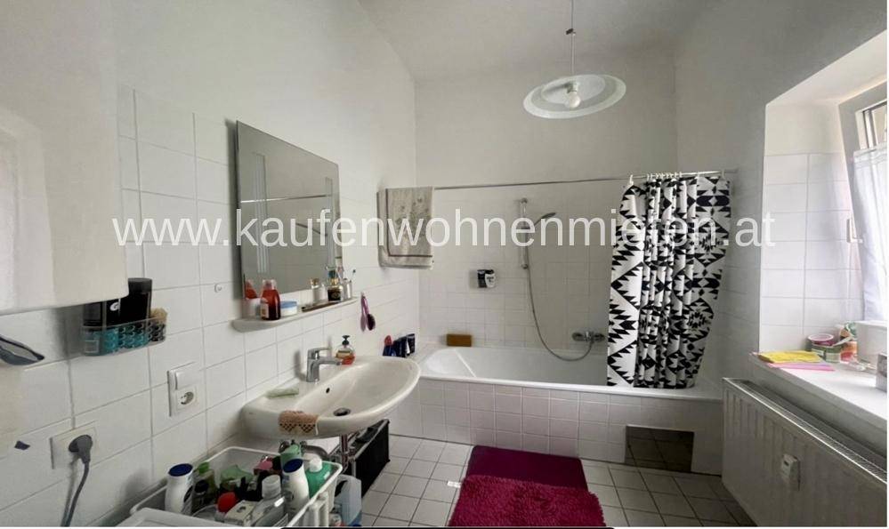 Helles Badezimmer mit Badewanne, Waschbecken und Fenster, ausgestattet mit weißen Fliesen.