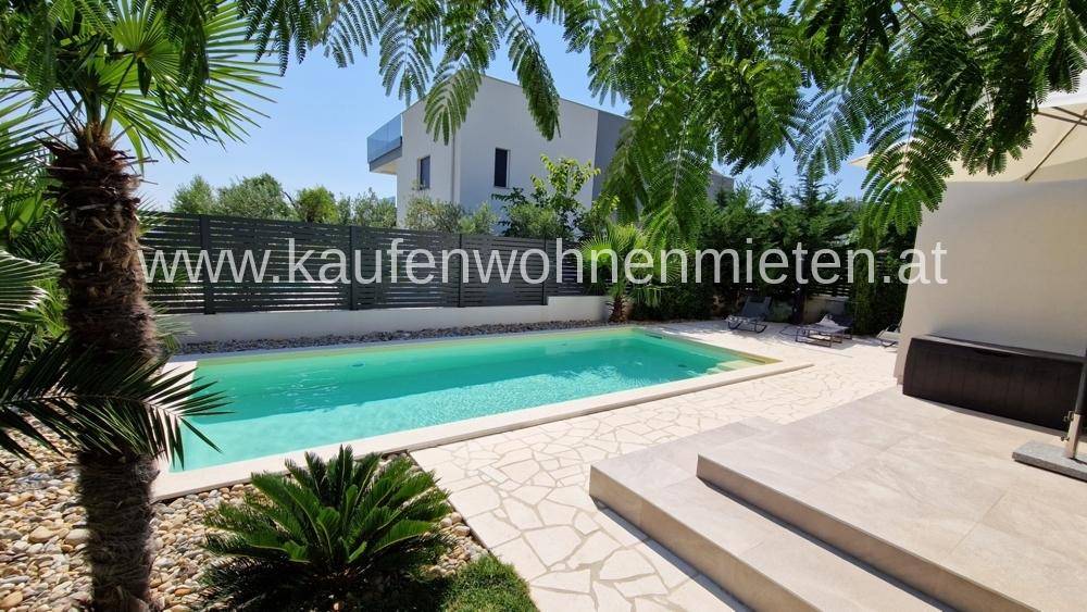 Entspannter Außenbereich mit Pool, Sonnenterrasse und schattenspendenden Bäumen vor der modernen Villa.