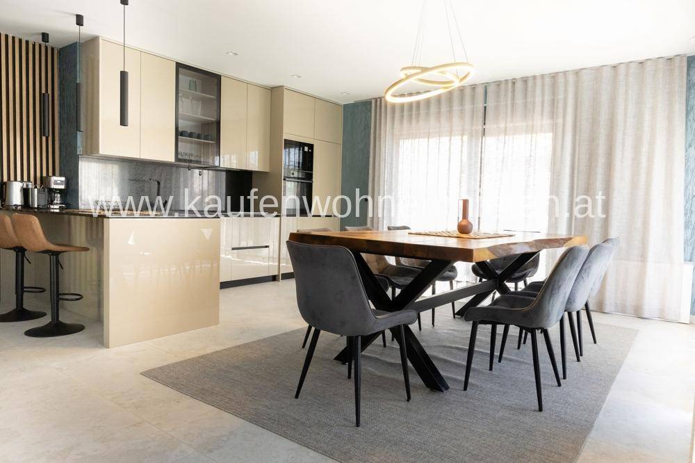 Moderne offene Küche mit beigen Hochglanzfronten und Essbereich mit Holztisch.