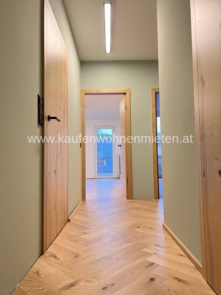Heller Flur mit Fischgrätparkettboden, hellgrünen Wänden und Holztüren.