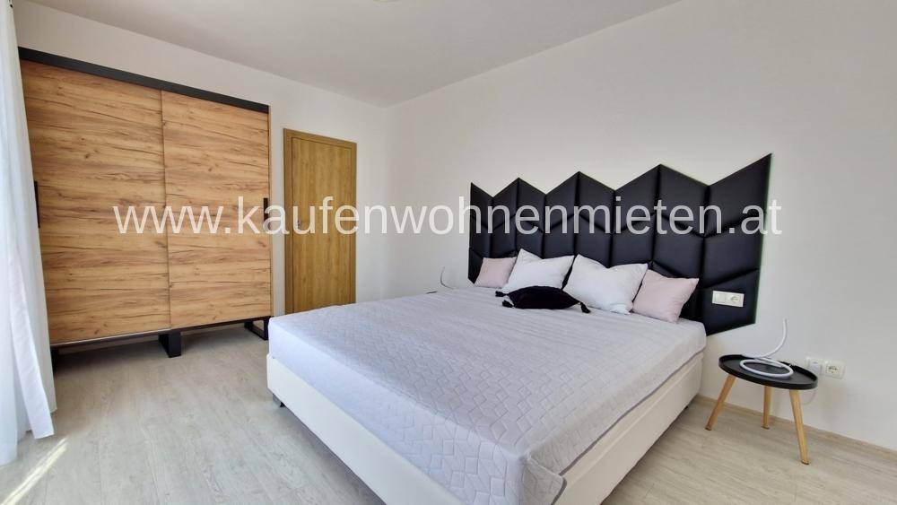 Geräumiges Schlafzimmer mit großem Bett, modernem Kopfteil und stilvollem Holzschrank.